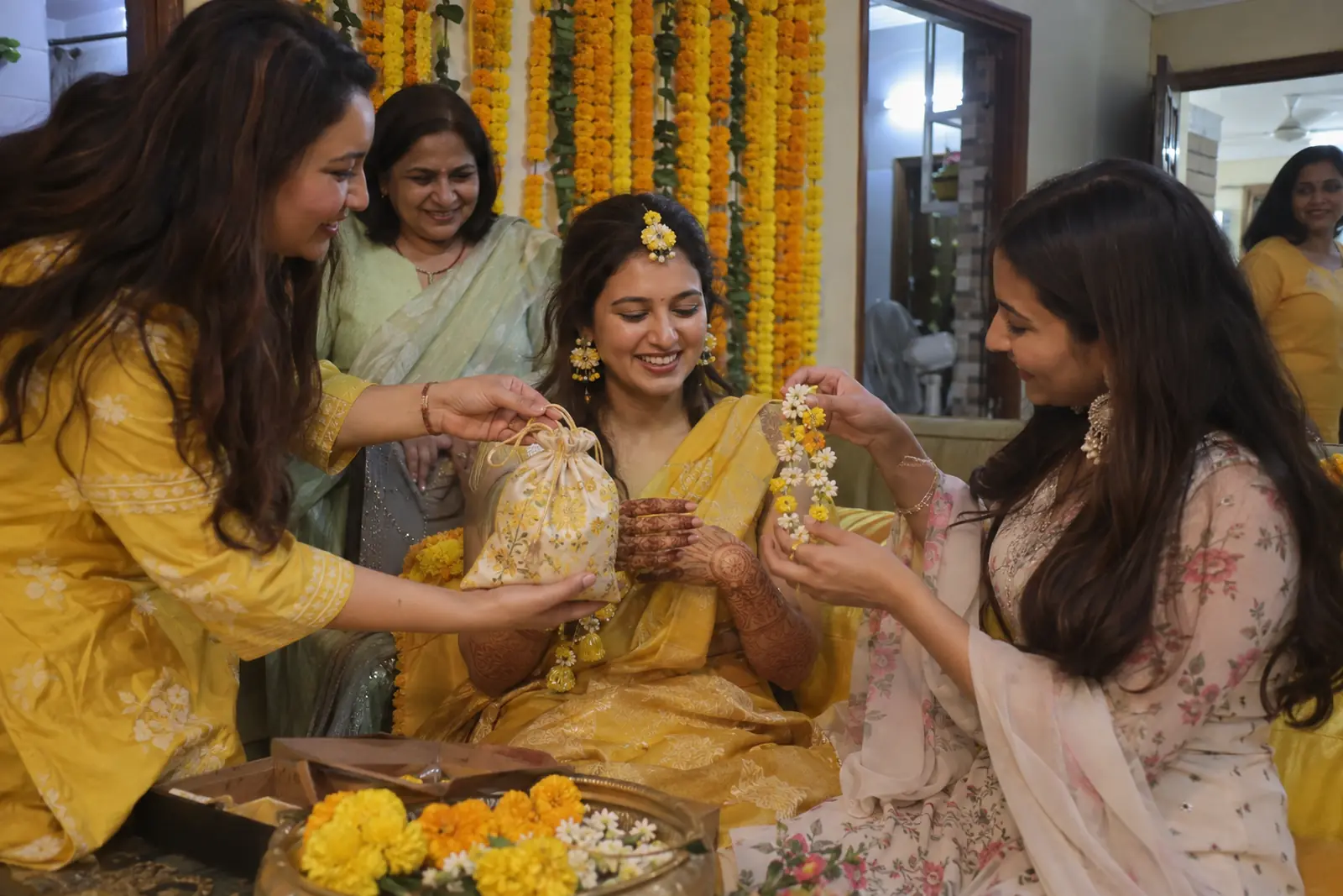 Friends give a bride with fresh mehendi a small potli and flower jewellery at a haldi setup