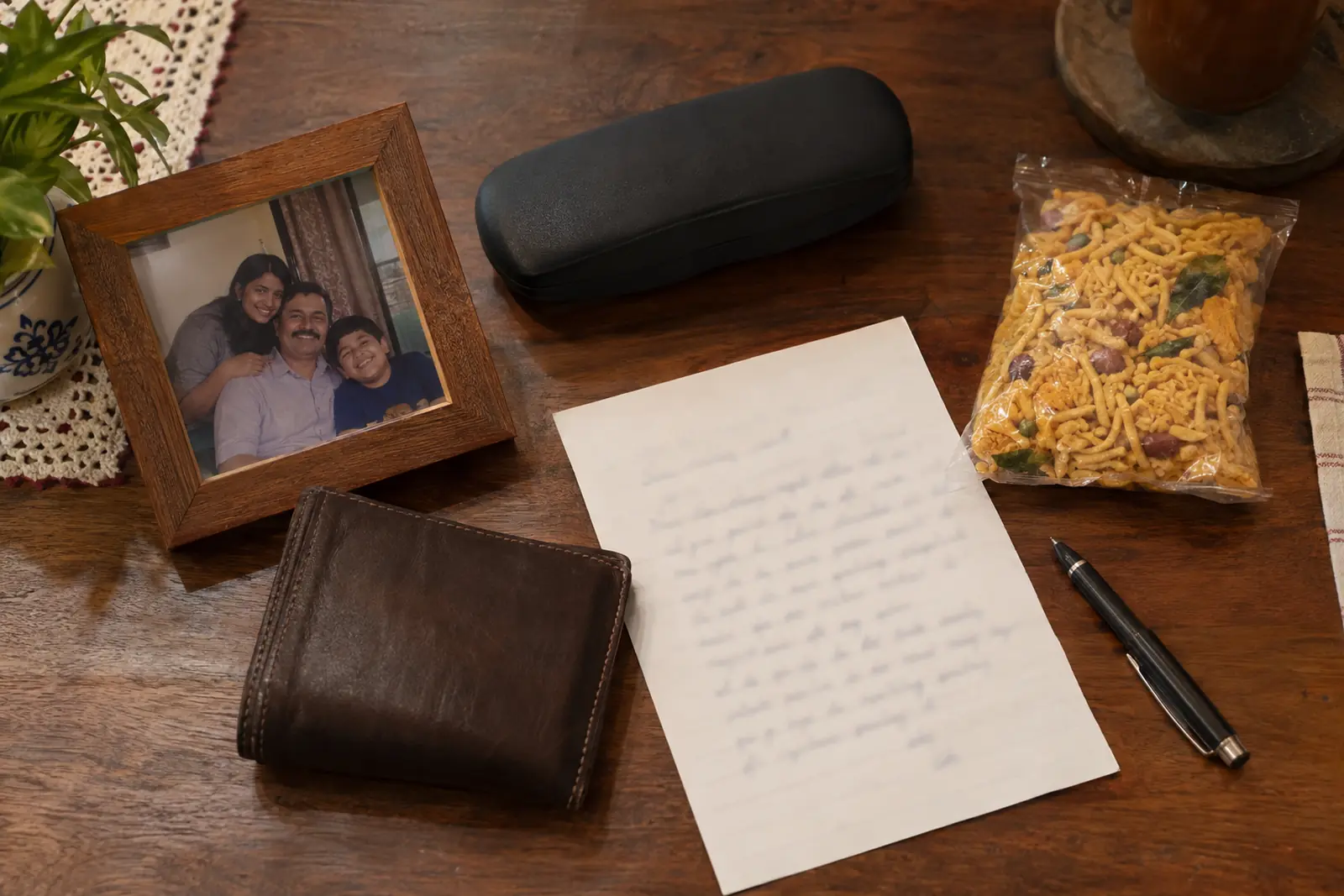 Flat-lay of small gifts for a father on a wooden table: a wallet, a handwritten letter, a spectacle case, namkeen and a photo frame