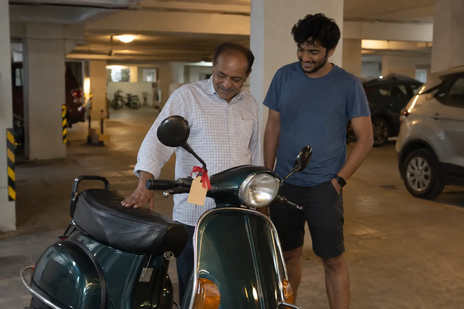 A son and his father look at the father's freshly serviced old scooter with a gift tag on the handlebar