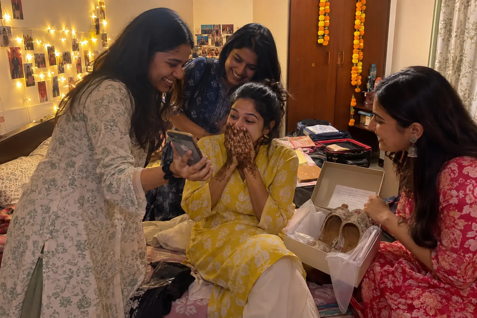 Friends surprise a bride with fresh mehendi on her hands with a gift box of juttis and a video on a phone